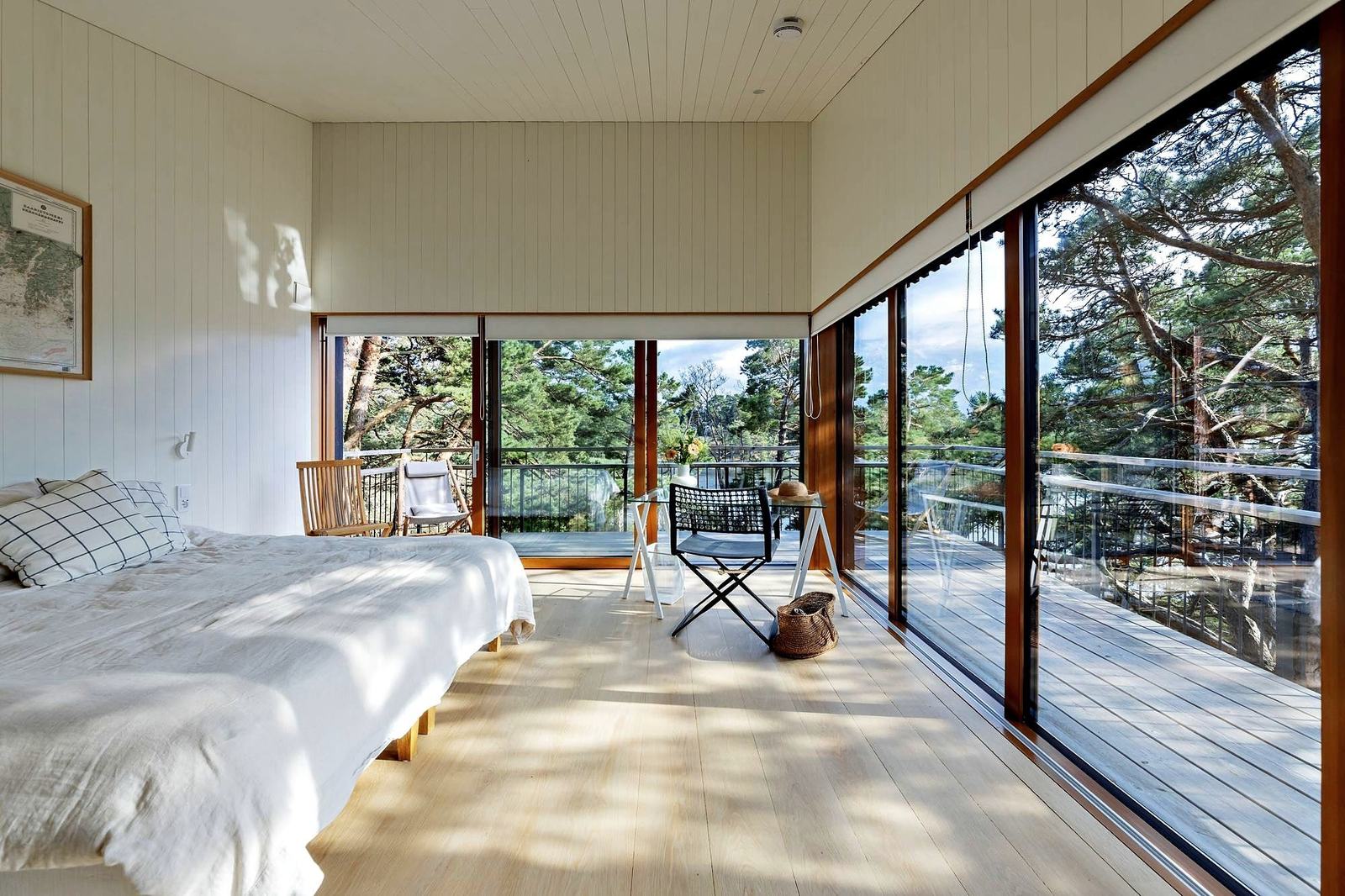 A double bed in a bright room, glass walls opening onto a terrace among the pines