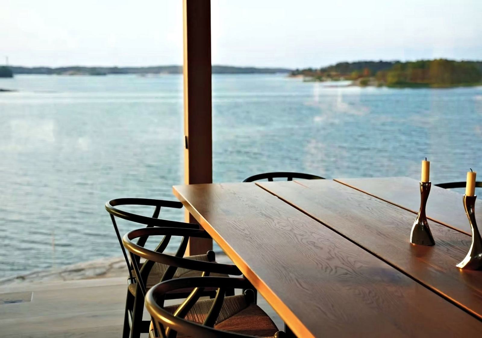 An oak dining table set with candles, facing the sea
